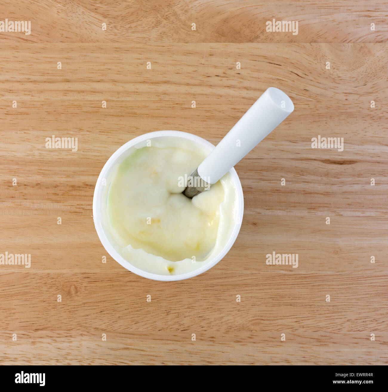 Top view of a small container of pineapple yogurt with a white handle spoon on a wood table top. Stock Photo
