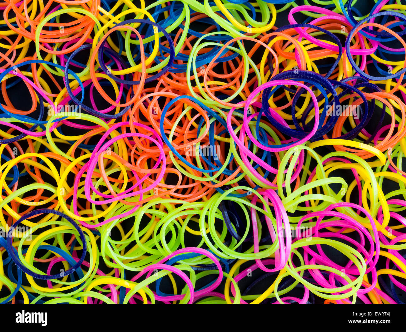 Close view of a group of neon hued rubber bands used for hair ponytails on a black background. Stock Photo