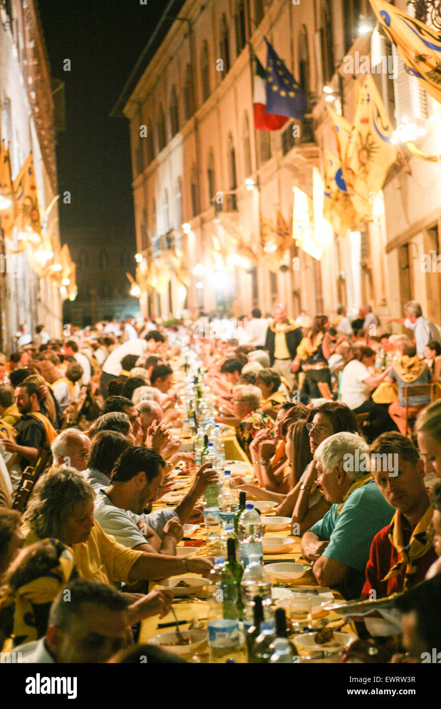 Eating dinner at a neighbourhood gathering. Siena is divided into 17 contrade neighbourhood districts and the neighbourhoods have a huge dinner the night before the main Palio horse race. In central Siena,Tuscany. Italy. July. Stock Photo