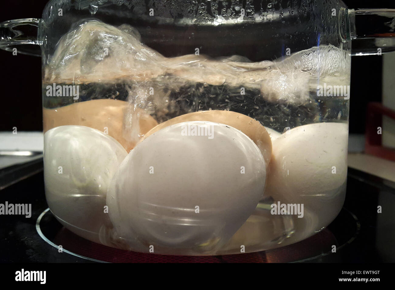 Boiling white and brown eggs in glass saucepan on the kitchen hot plate. Stock Photo