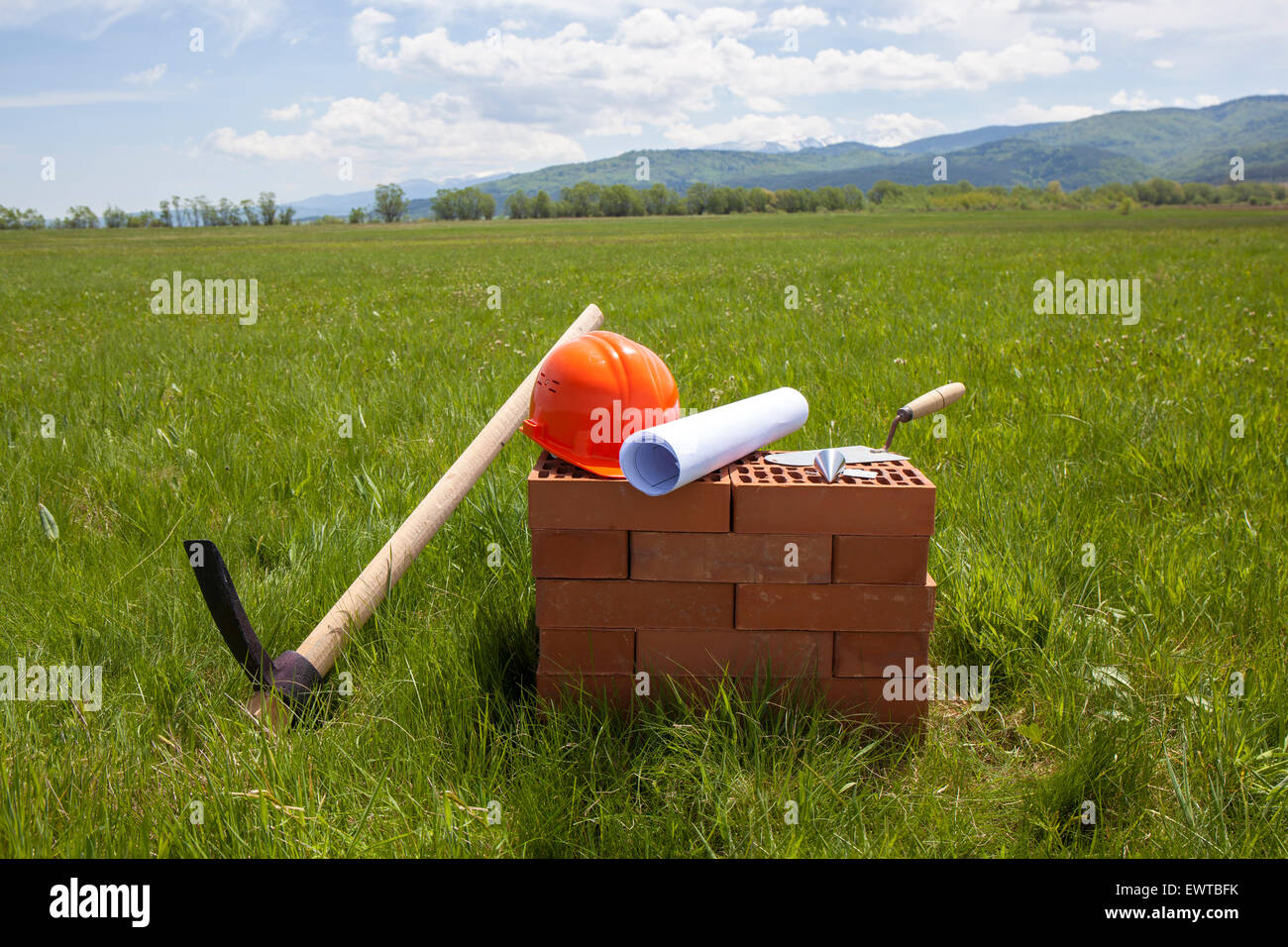 Bricks, trowel, blueprint on a roll, plummet, pick axe and hardhat prepared for beginning of construction of a new building. The Stock Photo