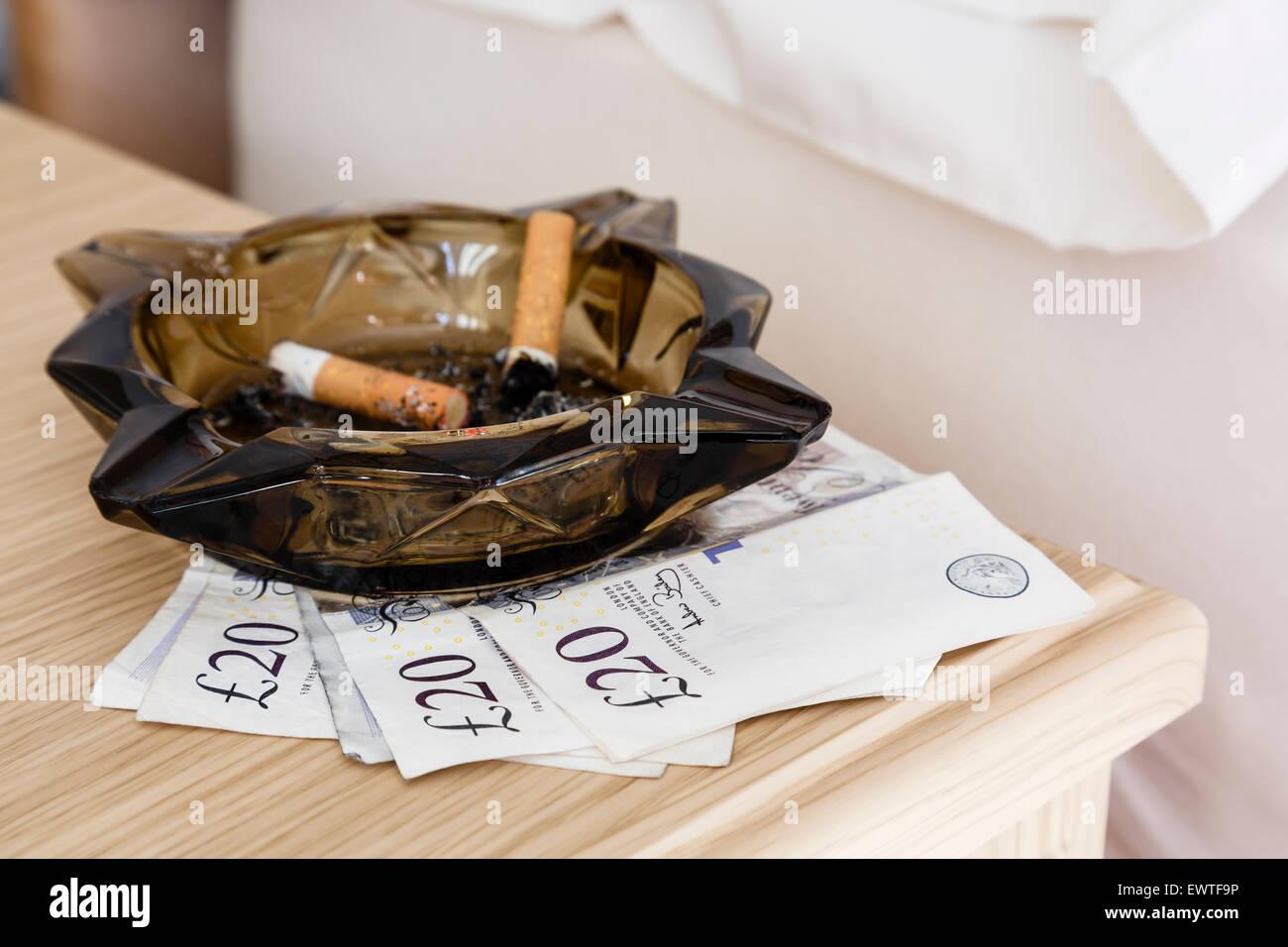 £60 notes left under an ashtray containing two cigarette stubs on a bedside table at side of a prostitute's bed to illustrate prostitution concept. UK Stock Photo