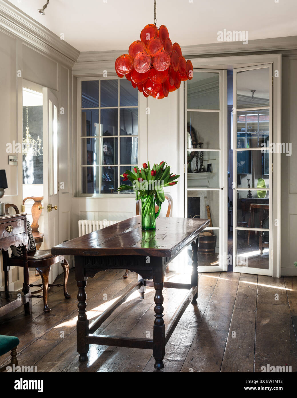 1960's red glass disc chandelier by Vistosi in panelled dining room with 18th century rectory table. Stock Photo