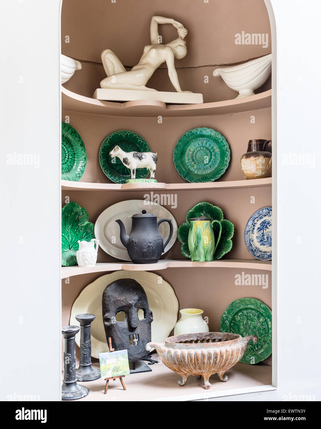 Green cabbage majolica plates alongside African pieces on alcove shelf. Stock Photo