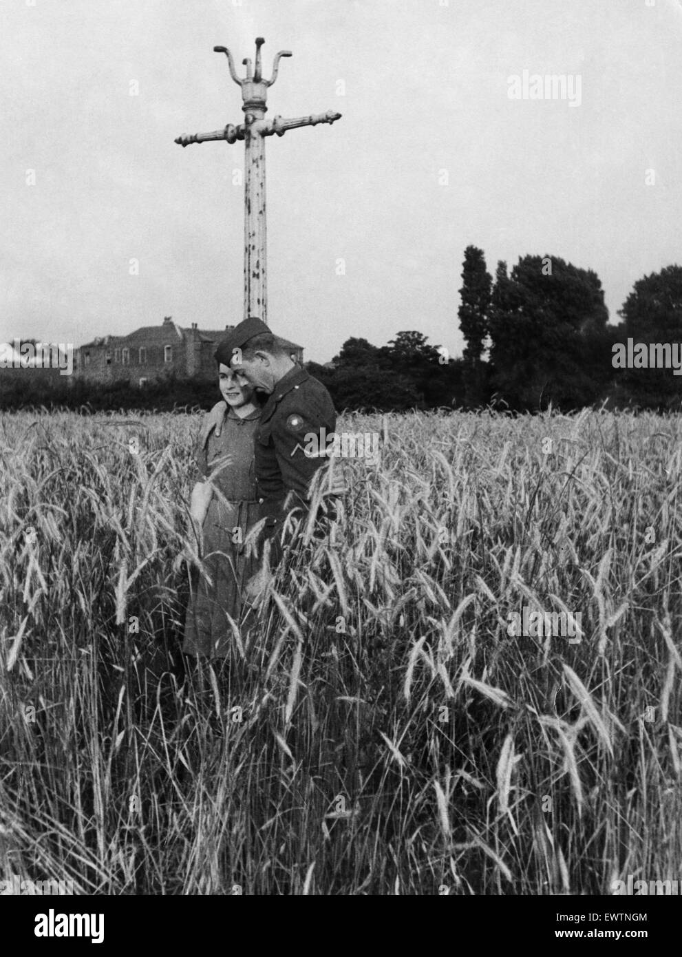 An American soldier and his girlfriend take a stroll through a field of barley near Maryvale, Birmingham. The lamp post is all that remains of a planned housing estate which was cancelled at the beginning of the war and the land turned over to food produc Stock Photo