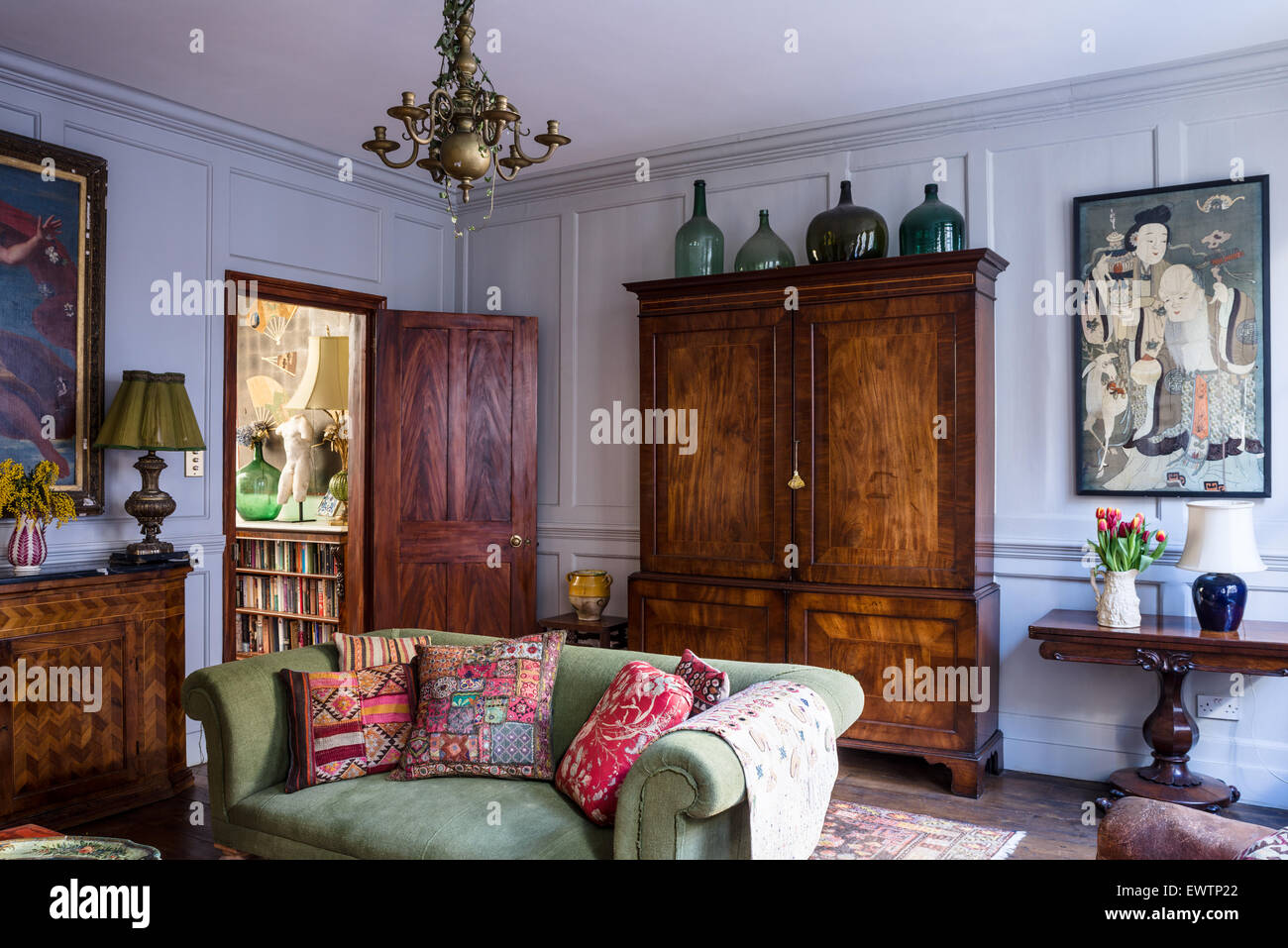 Indian and antique French cushions on green sofa in living room with large antique armoire and oriental artwork Stock Photo