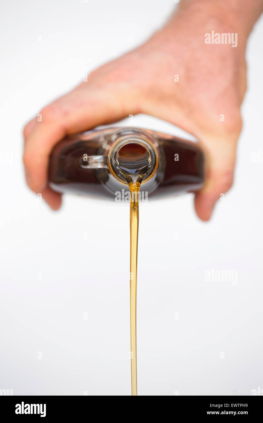 Hand pouring Organic American Maple syrup from a bottle against white