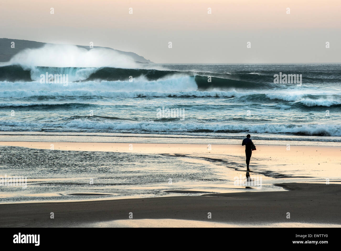 Bodysurfer standing on the beach at sunset in Cornwall after surfing big waves. Stock Photo