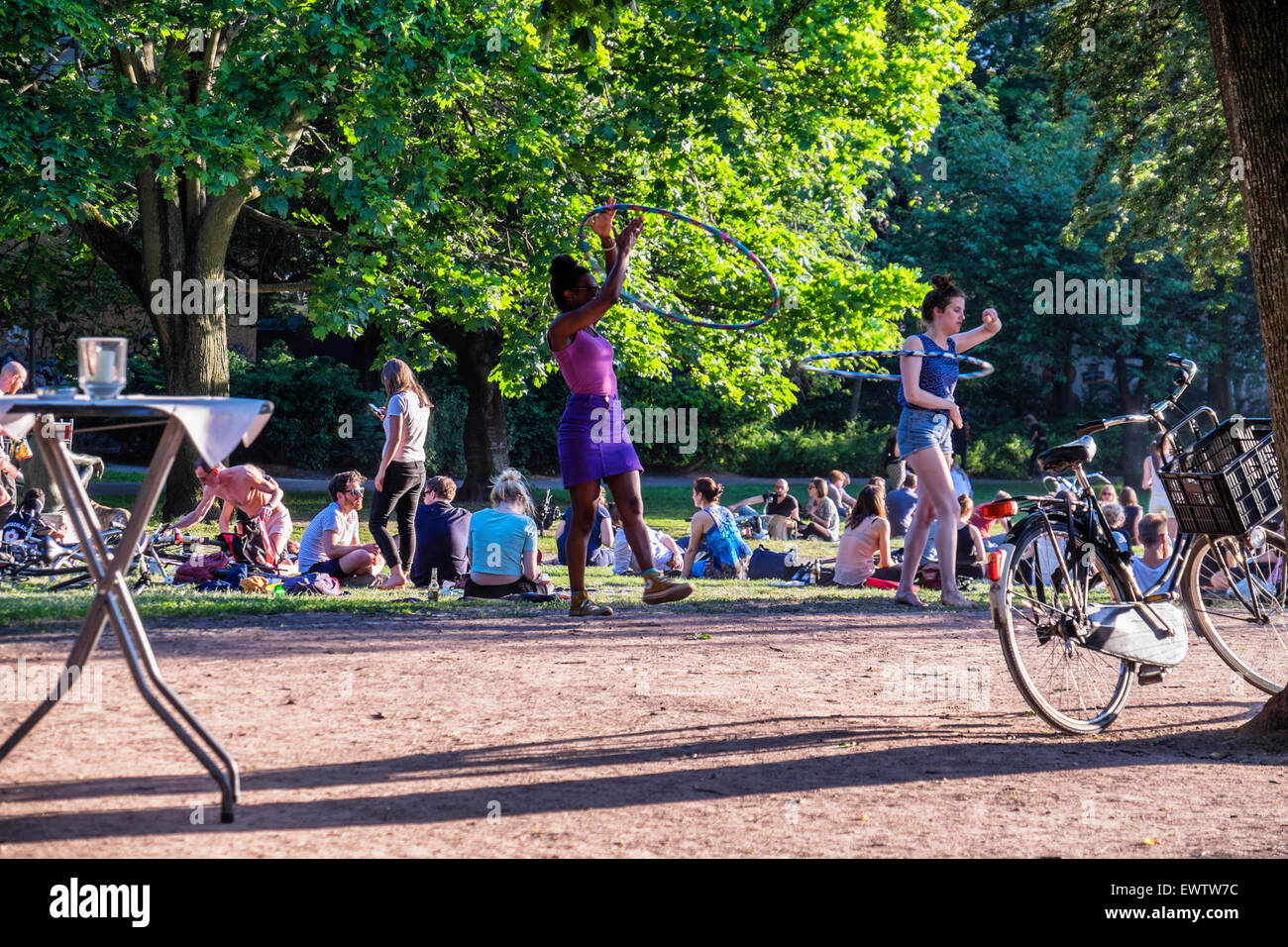 Two young woman hula hooping as people relax in Berlin Public Park in warm summer weather, Volkspark am Weinbergstrasse Stock Photo