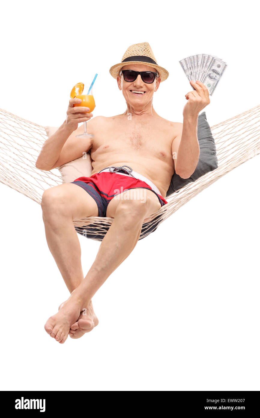 Vertical shot of a joyful senior man in a swim trunks drinking a cocktail and holing a stack of money seated in a hammock Stock Photo