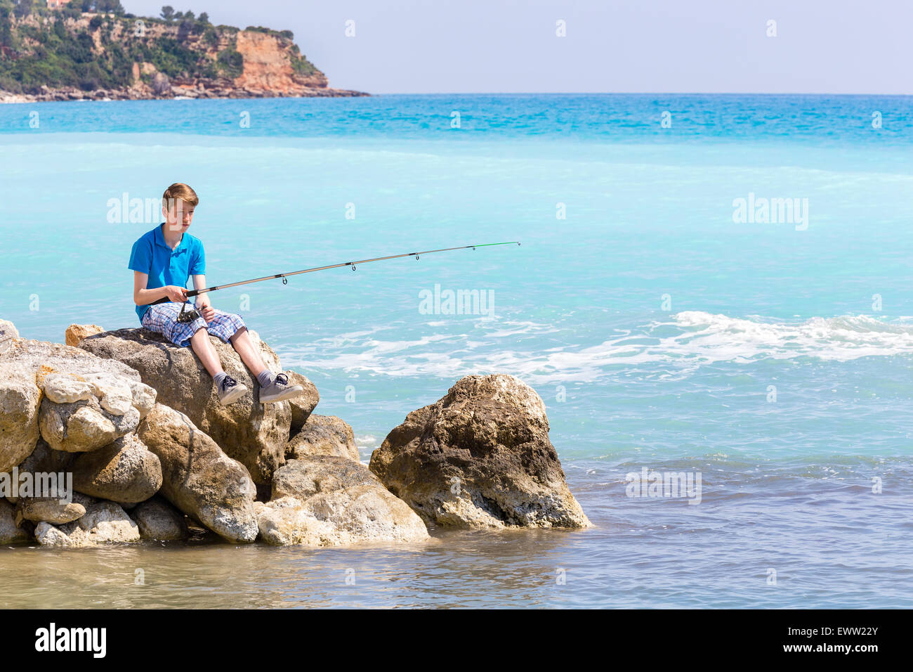 Caucasian teenage boy fishing with rod near sea and beach Stock Photo