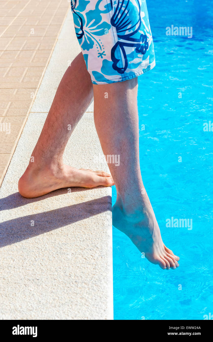 Legs of teenage boy with foot feeling water tempaeature in swimming pool on  sunny day in summer Stock Photo - Alamy