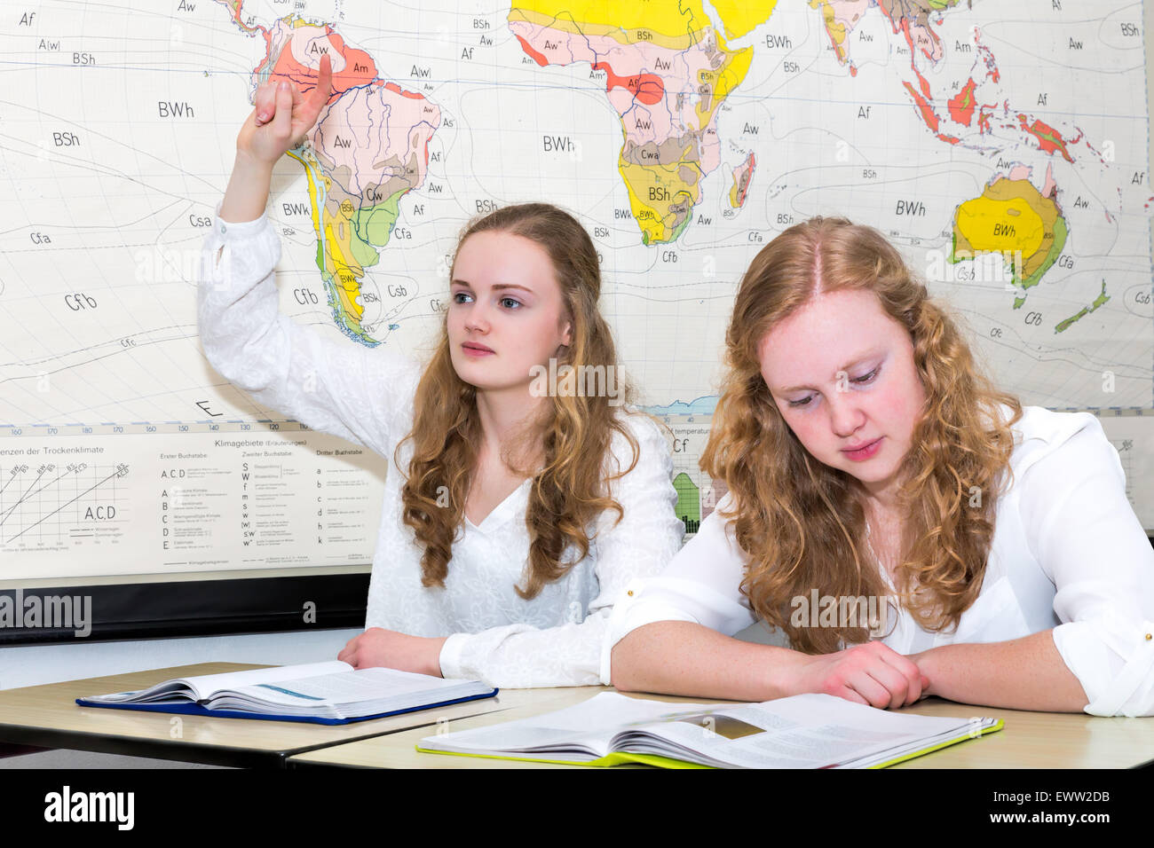 Caucasian teenage girl and student with learn finger in geography lesson in front of wall chart of the world Stock Photo