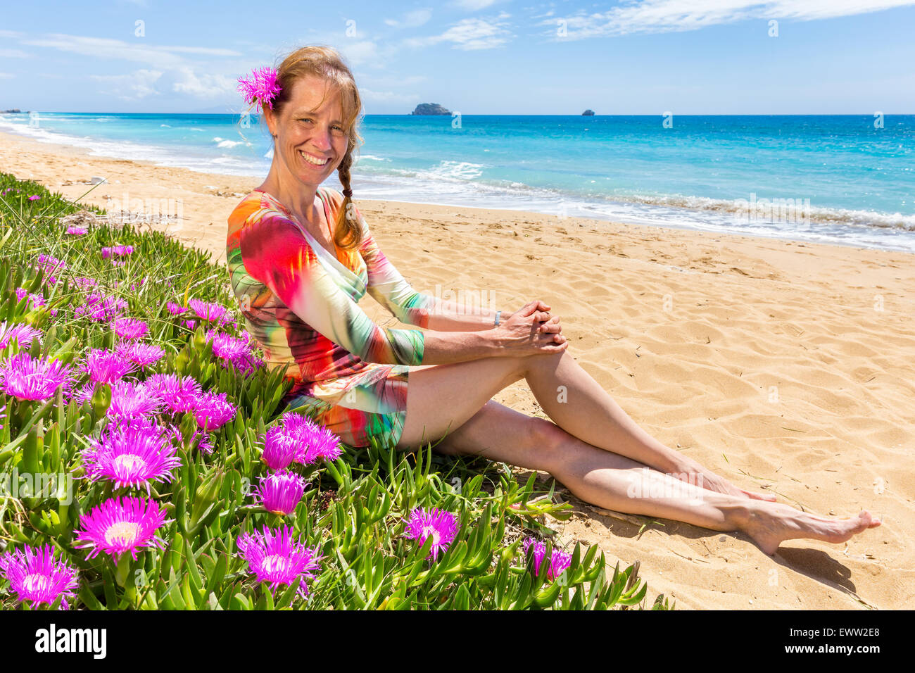 Woman with pink flowers on sandy beach with blue sea Stock Photo