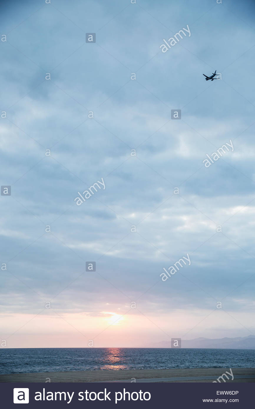 Plane in overcast sunset sky over ocean Stock Photo