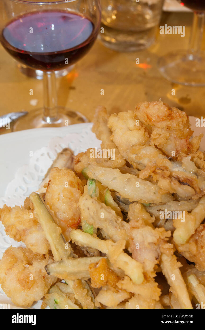 fish fry, vegetables and glass of red wine in italian restaurant Stock Photo