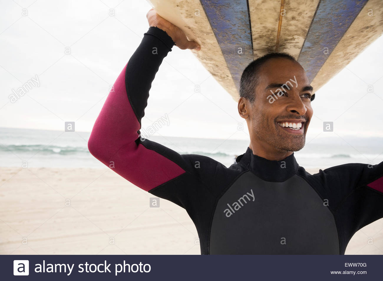 Smiling man in wetsuit holding surfboard overhead Stock Photo Alamy