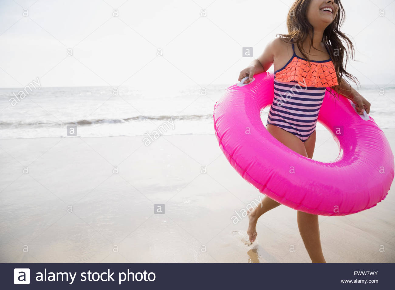 Girl running with pink inflatable ring on beach Stock Photo