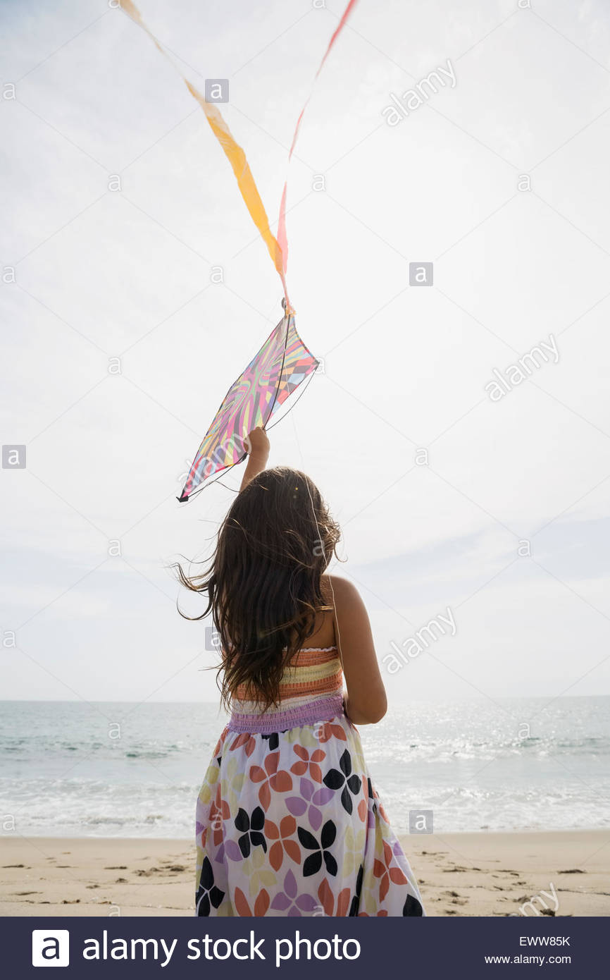 Girl in dress flying kite on sunny beach Stock Photo