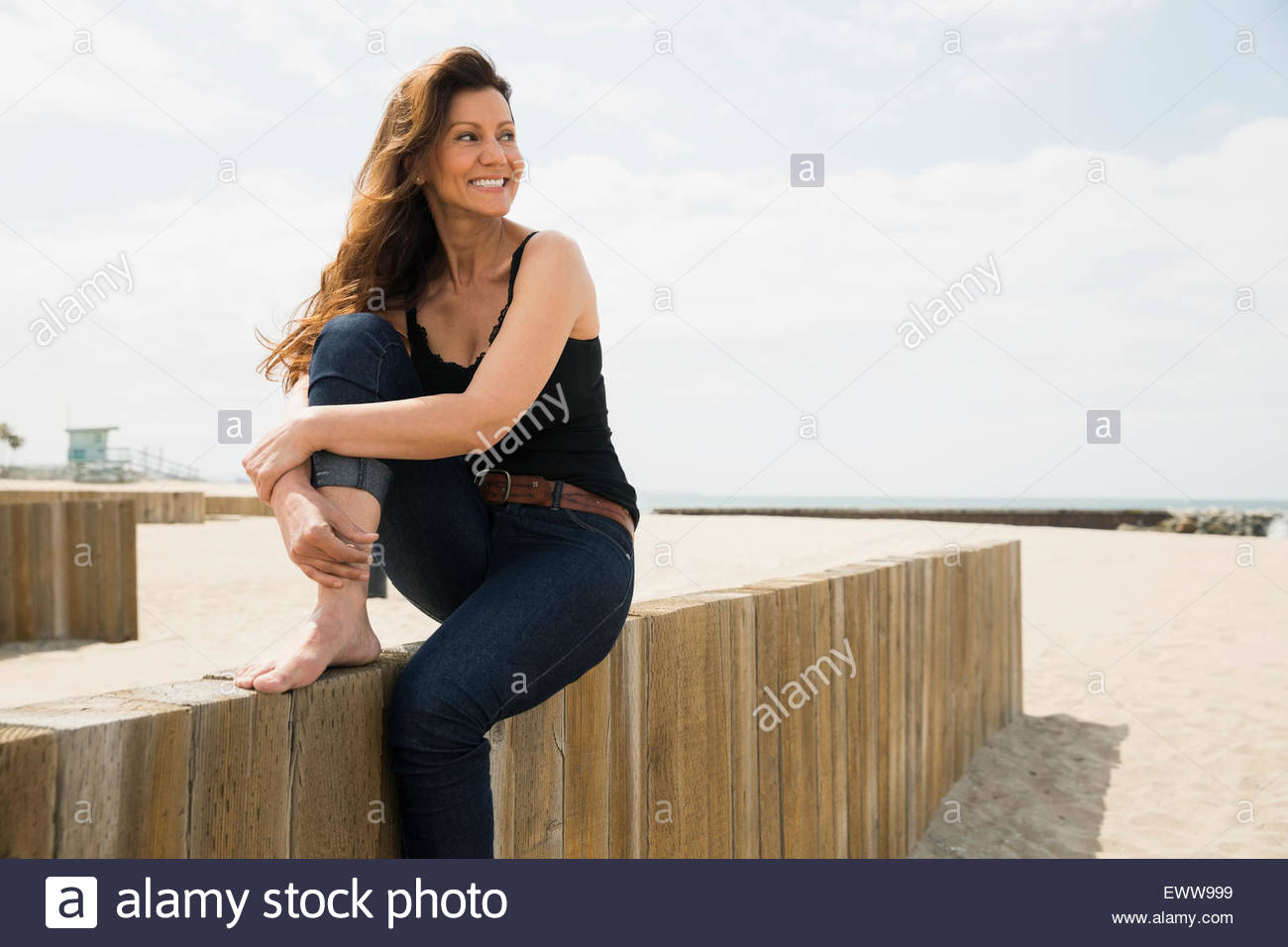 Smiling barefoot woman sitting on beach wall Stock Photo