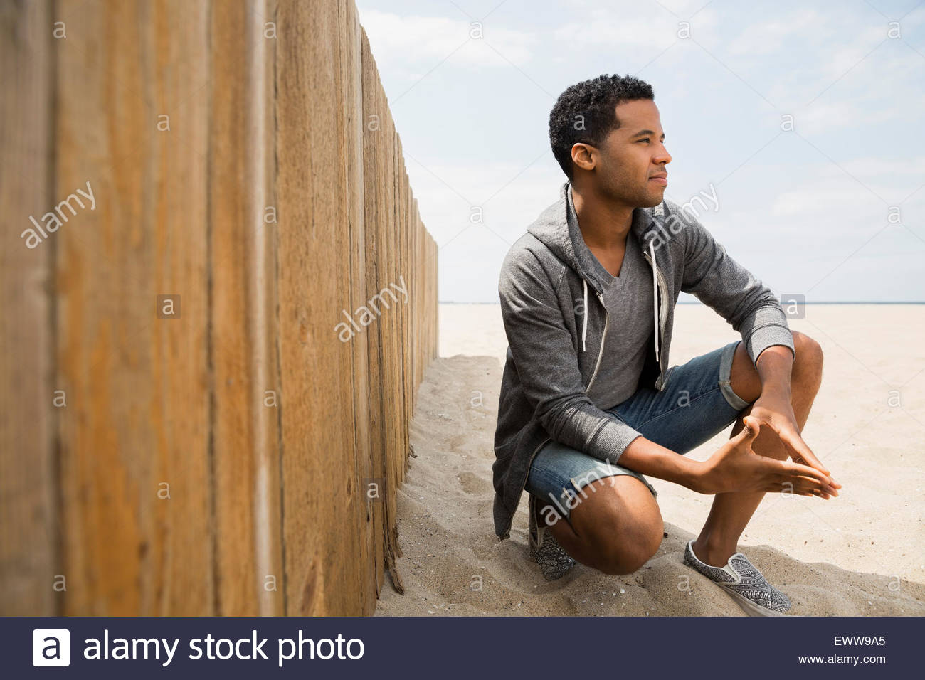 Man crouching on beach along wall Stock Photo