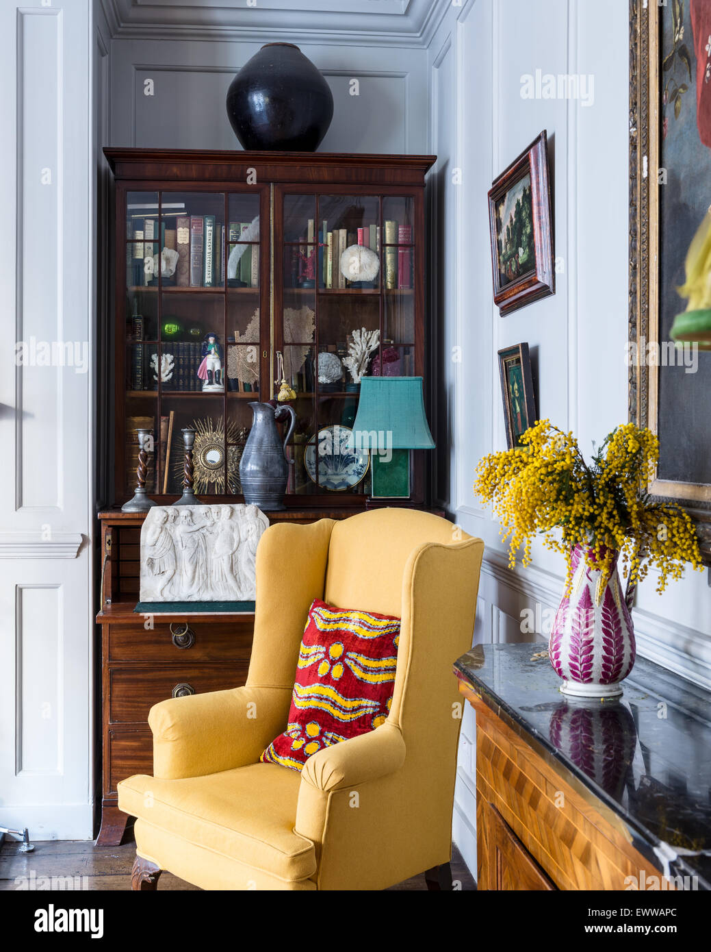 Yellow wingback armchair in front of walnut display cabinet in panelled sitting room Stock Photo