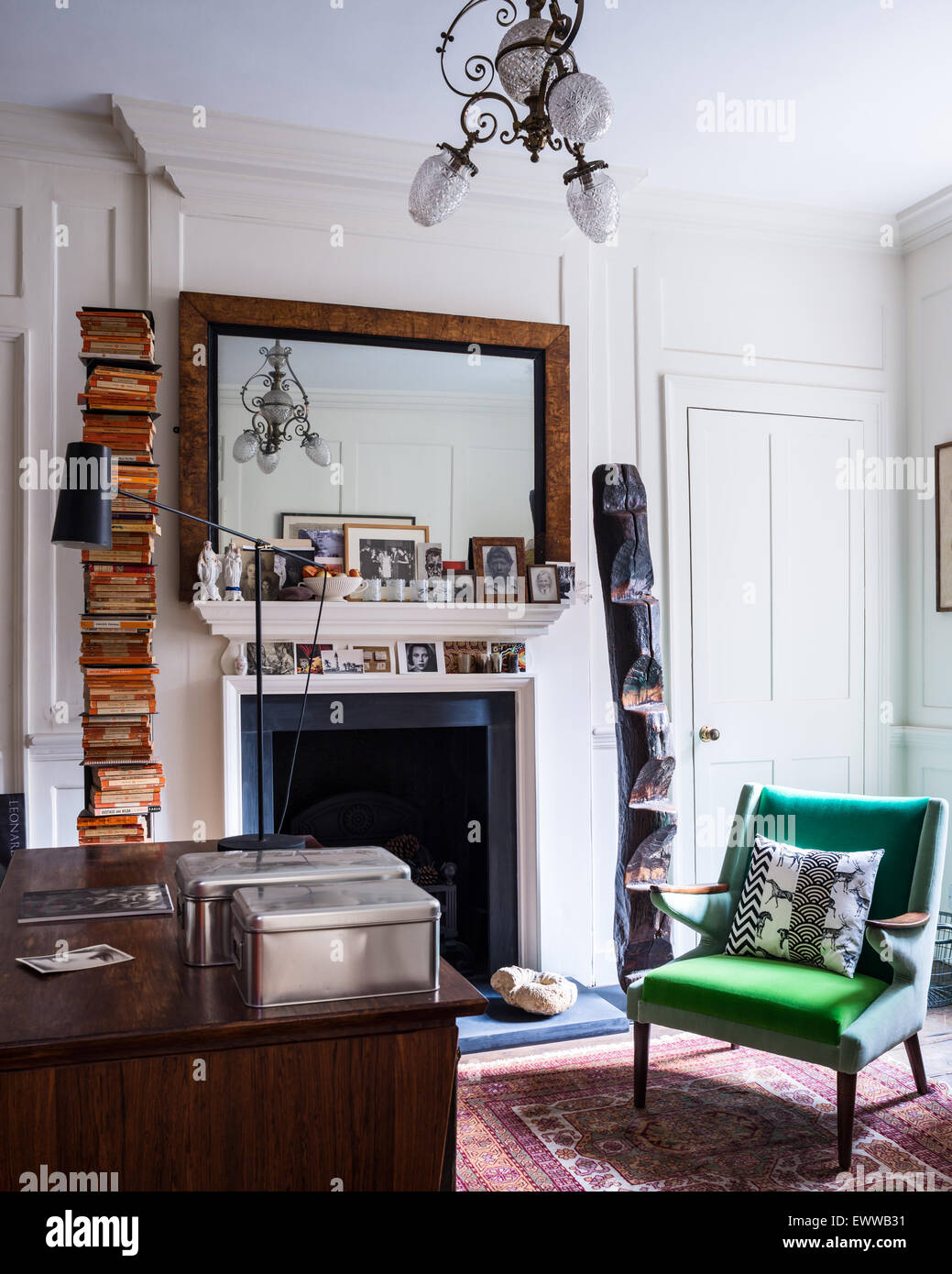Mid century green armchair in study with persian rug, mantelpiece and stacked books Stock Photo