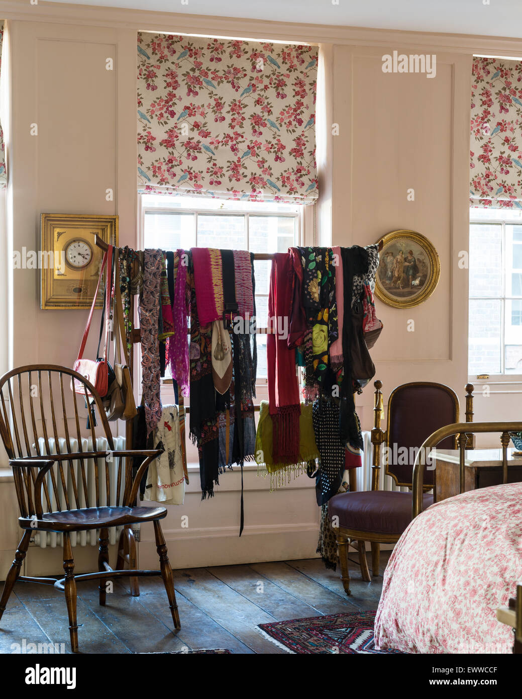 Assorted scarves hung on a chinese clothes rack in bedroom with floral patterned blinds and windsor chair Stock Photo