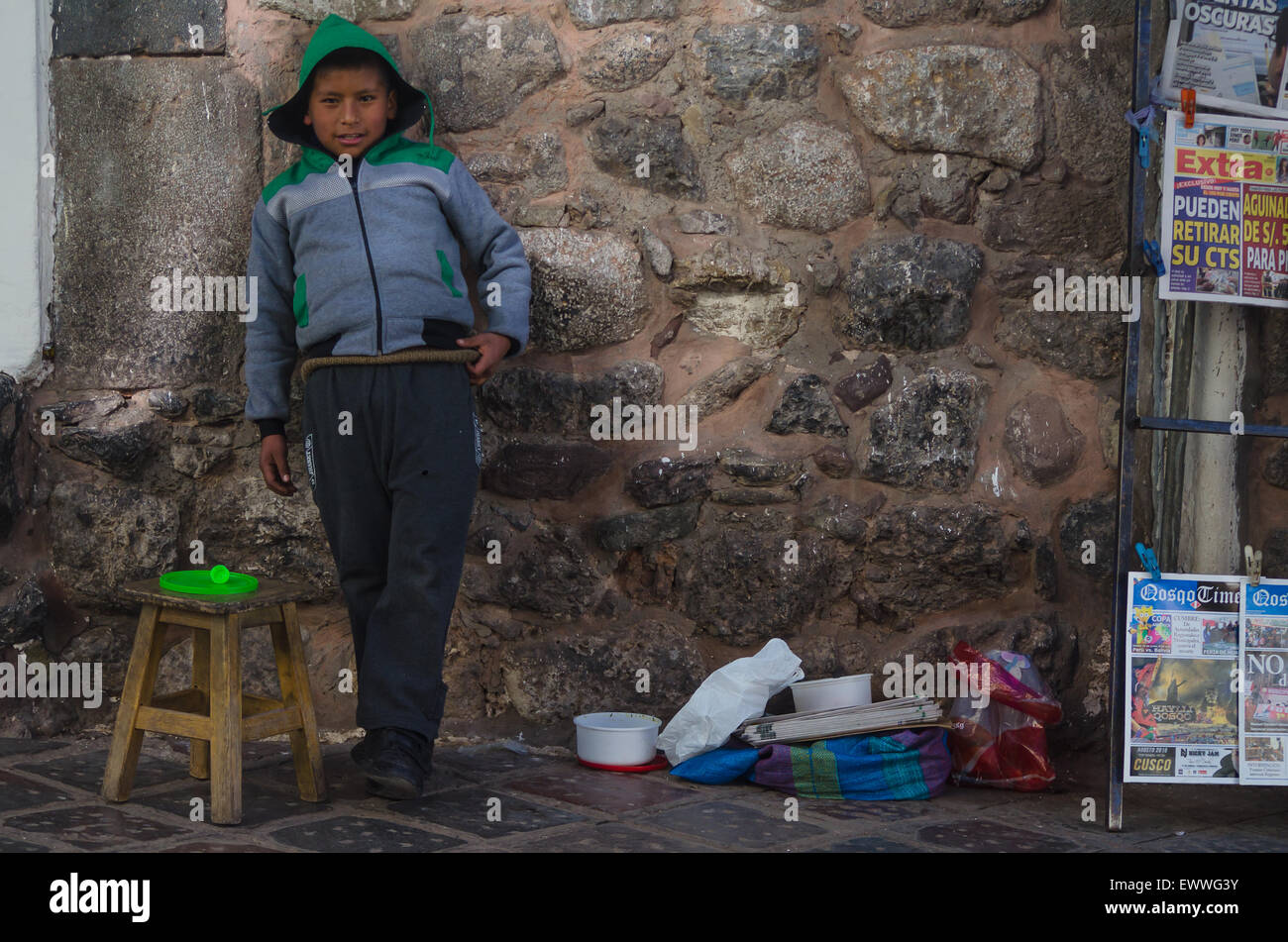 Boy standing against a stone wall in Cusco, Peru, selling items. Stock Photo