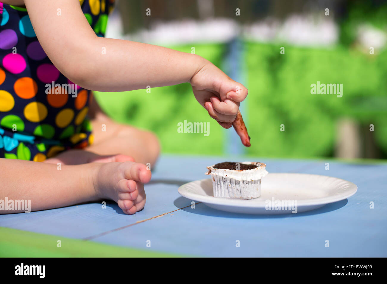 Cute baby wearing spotted swimsuit tasting a cupcake with her finger Stock Photo