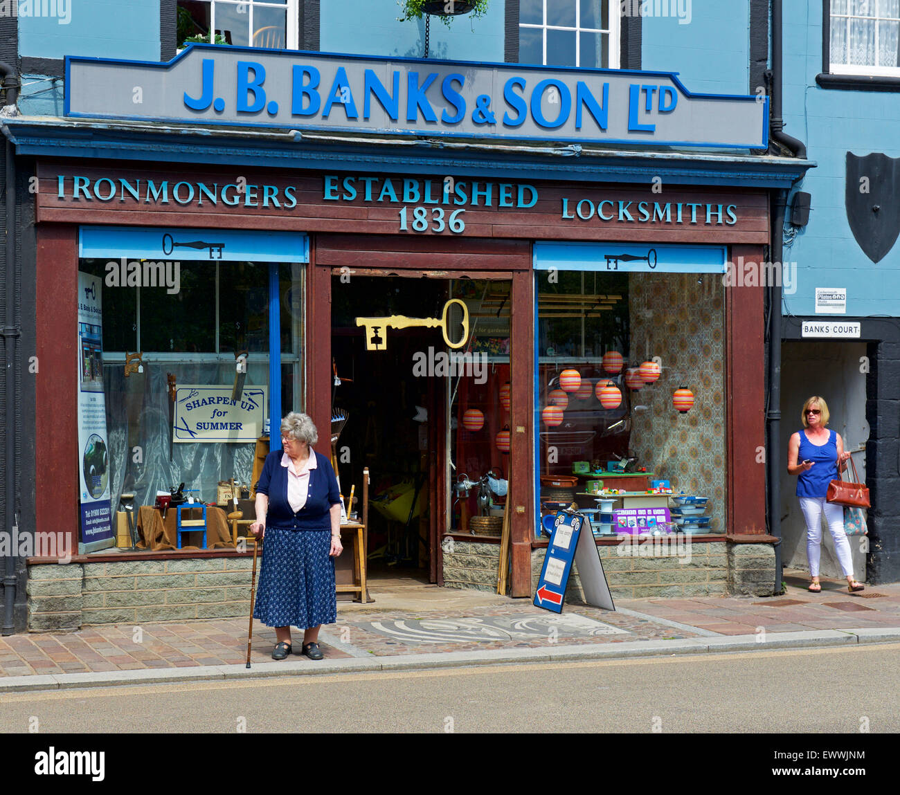 Elderly woman standing in front of ironmongers shop, Cockermouth, West Cumbria, England UK Stock Photo