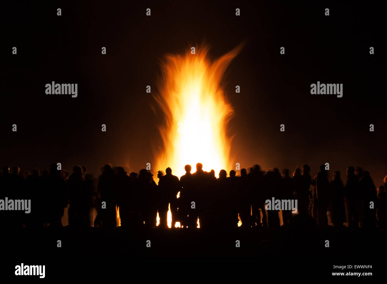 Silhouttes of a group of people watching a bonfire set against the flames and black night Stock Photo