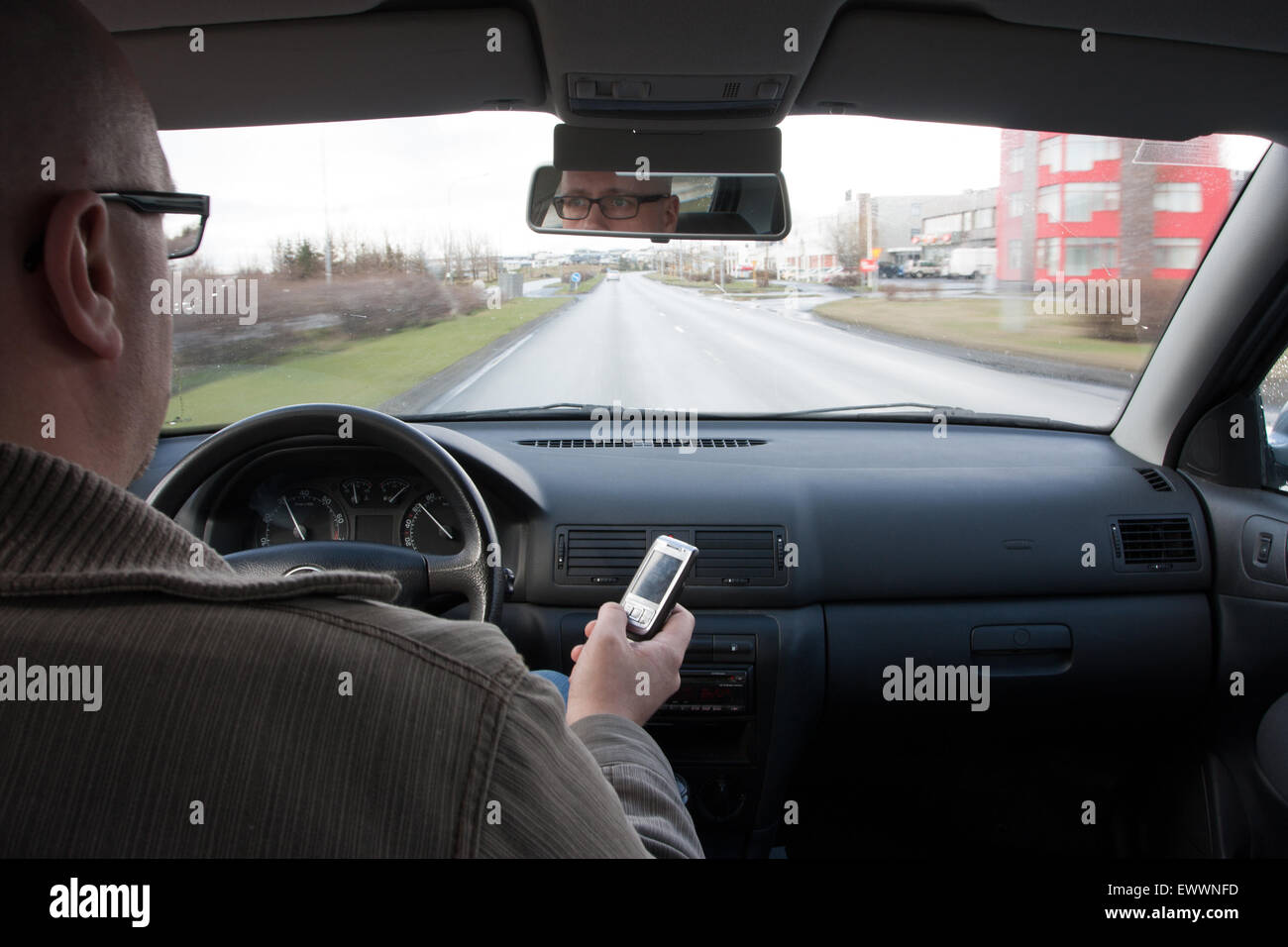 Man messaging on mobile while driving, shot from the backseat Stock Photo