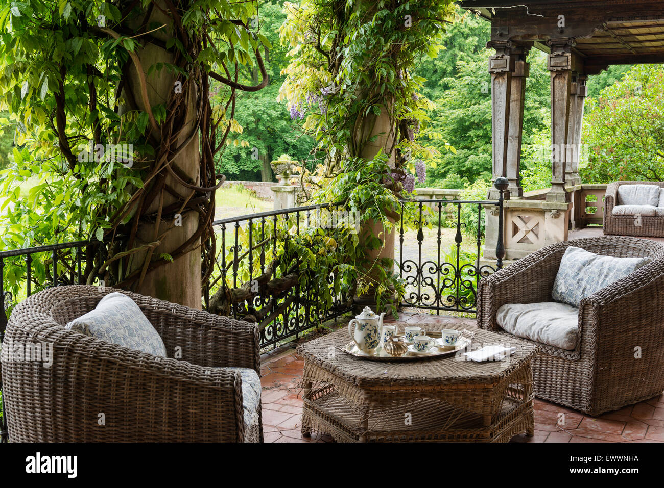 Wicker garden furniture on terrace with wisteria-clad columns and iron balustrade Stock Photo