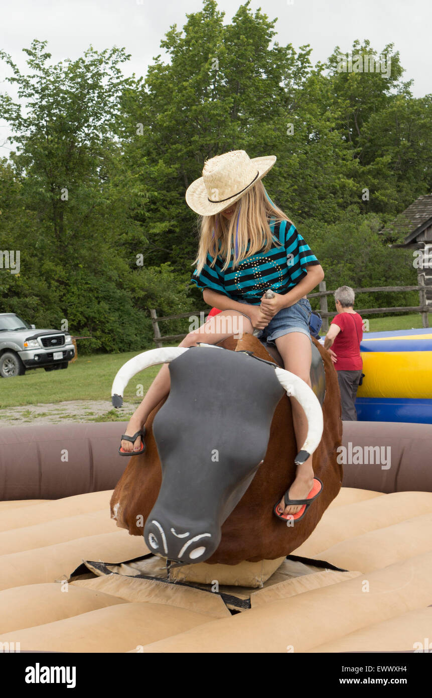 Young pre-teen girl rides a mechanical bull at the Canada Day celebrations in Cannington, Ontario Stock Photo