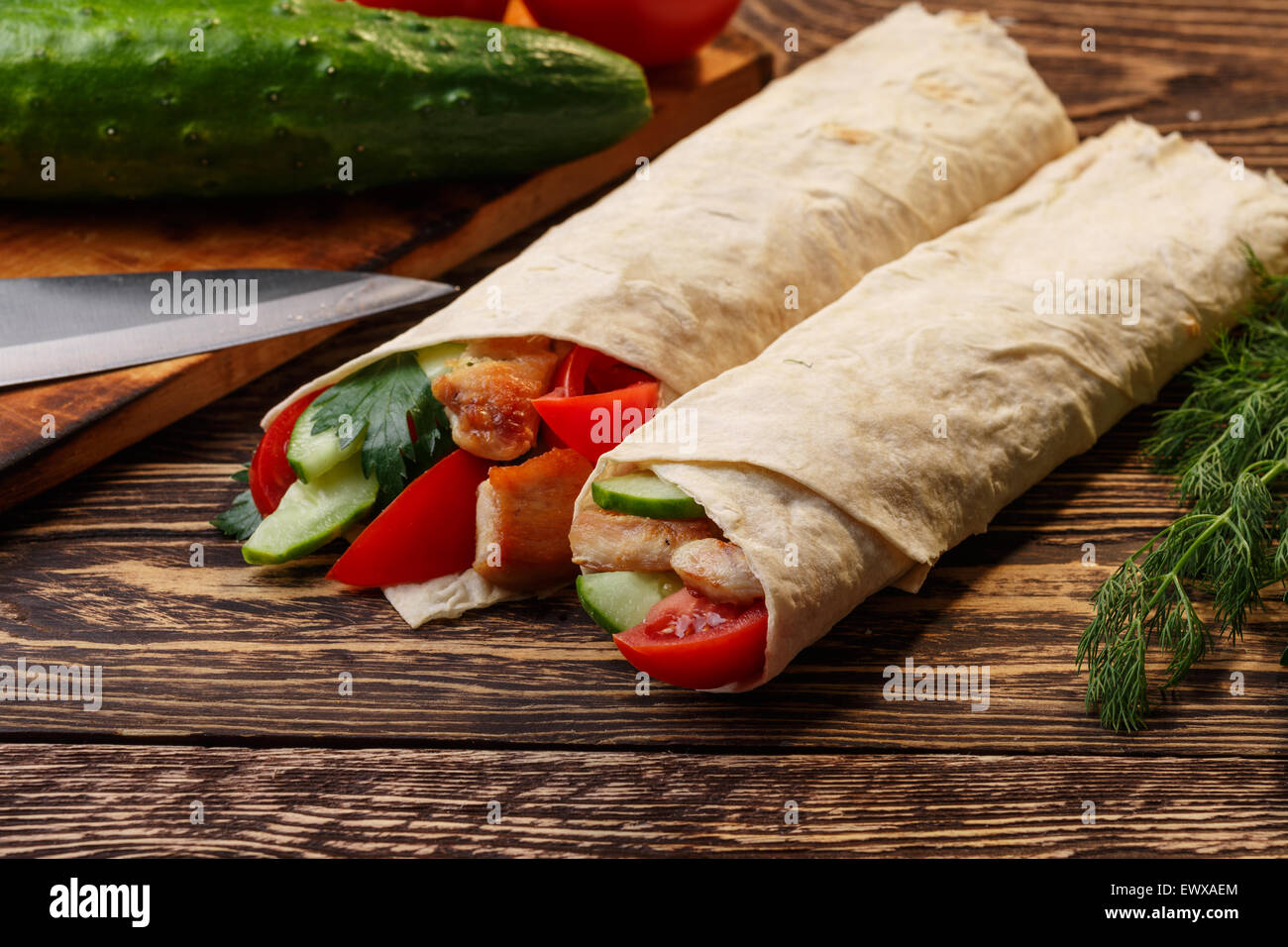 Traditional shawarma wrap with chicken and vegetables near cutting table Stock Photo