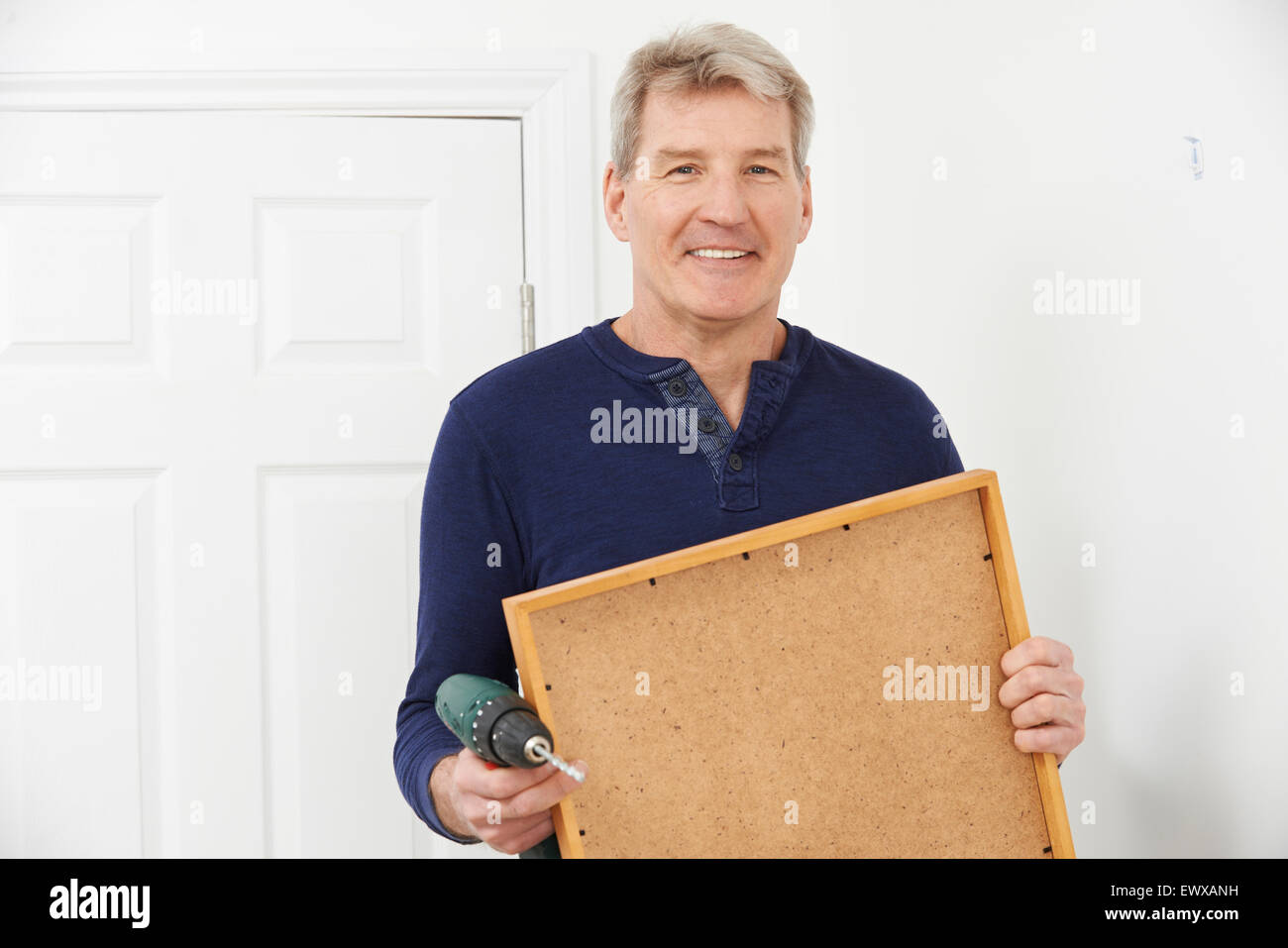 Mature Man Drilling Wall To Hang Picture Frame Stock Photo
