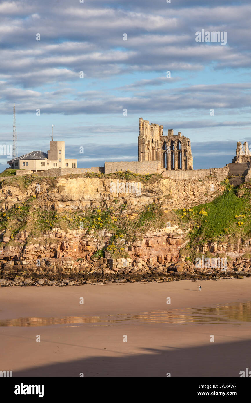 Castle, Abbey and Coastguard watch station on the cliffs at Tynemouth. A lone walker strolls on the sands in low evening light. Stock Photo