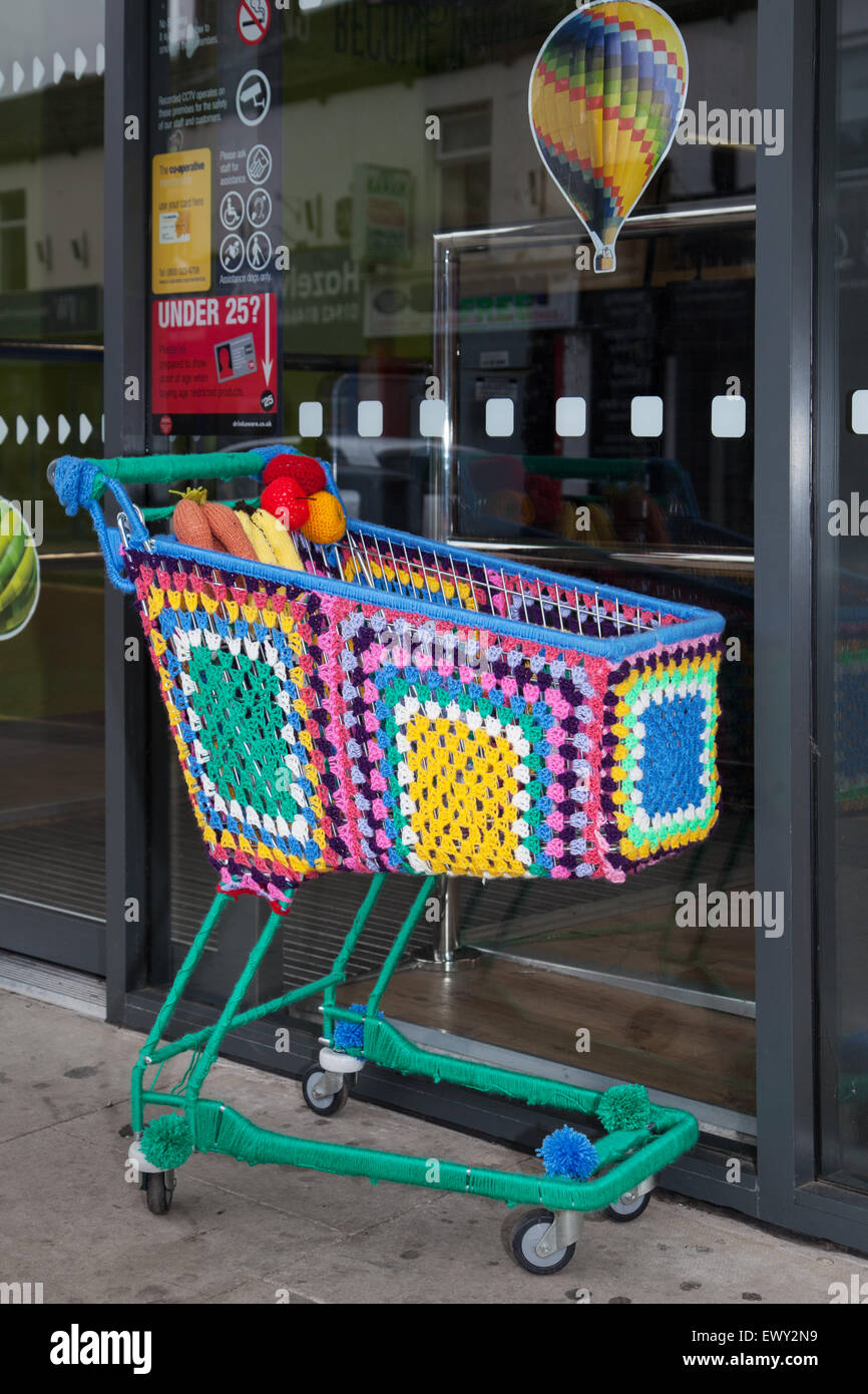 Yarn-bombed, bombing, yarnbombing, colourful decorative knitted, Co-op Supermarket shopping Trolley, wire cart, Westhoughton, Lancashire, UK Stock Photo