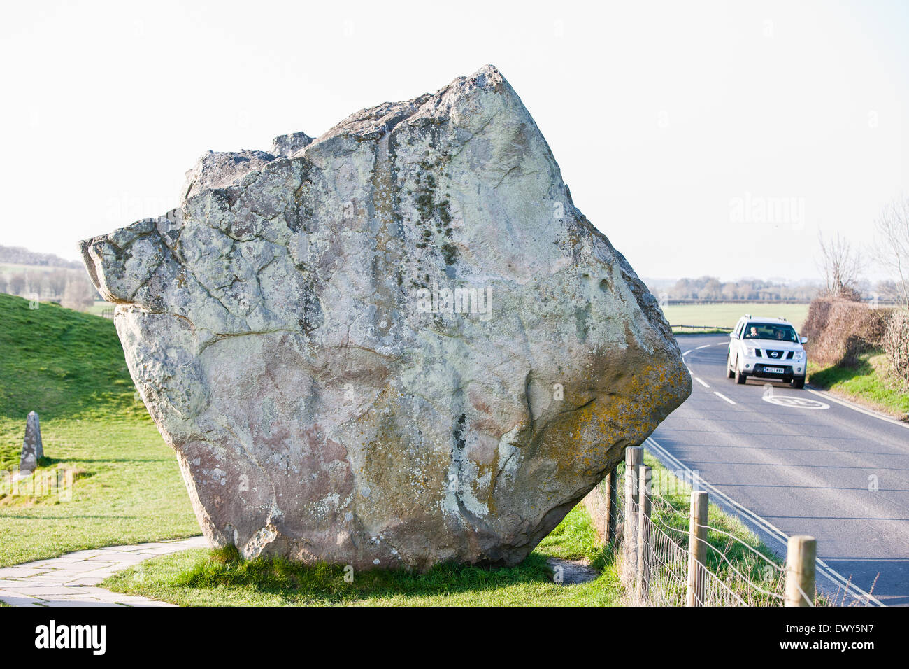 Huge stone and passing car on road at Avebury. Avebury a UNESCO World Heritage Site is a Neolithic Henge monument containing 3 stone circles around village of Avebury in Wiltshire. Unique amongst megalithic monuments, Avebury contains the largest stone circle in Europe, and is one of the best known pre-historic sites in Britain. Constructed around 2600 BC it is both a tourist attraction and a place of religious importance to contemporary pagans. Wiltshire, England, Europe. Stock Photo