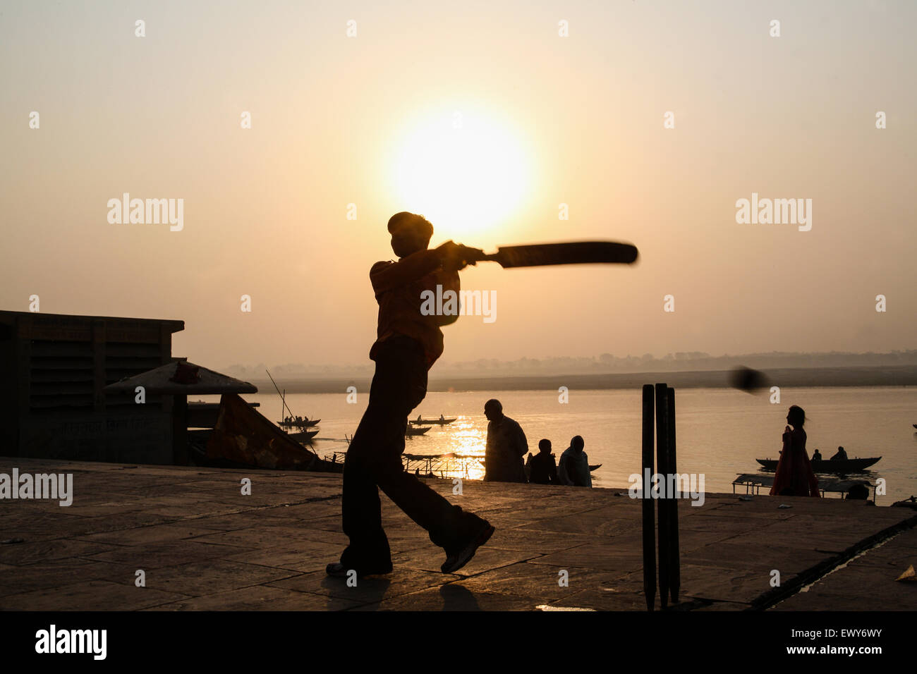 Local boys, on bathing ghat, playing popular national sport of cricket at sunrise. A good hit and the ball goes into the River Ganges. The culture of Varanasi is closely associated with the River Ganges and the river's religious importance.It is 'the religious capital of India'and an important pilgrimage destination.Varanasi, also known as Benares, an ancient city, one of the world's oldest continually inhabited cities, situated on the left/west bank of the sacred Ganges River. Regarded as holy by Hindus, Buddhists, and Jains. Uttar Pradesh State, India, Asia. Stock Photo