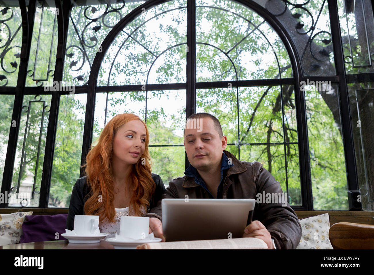 Two students drinking coffee and having fun with tablet In cafeteria Stock Photo