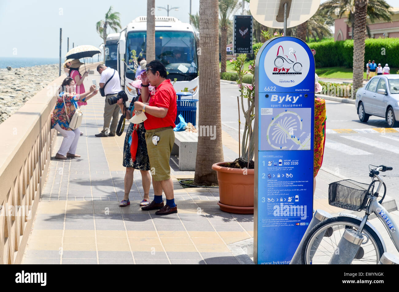 Chinese tourists visiting Dubai, UAE, on Palm Jumeirah artificial island, naer a Byky sign for bicycle rental Stock Photo