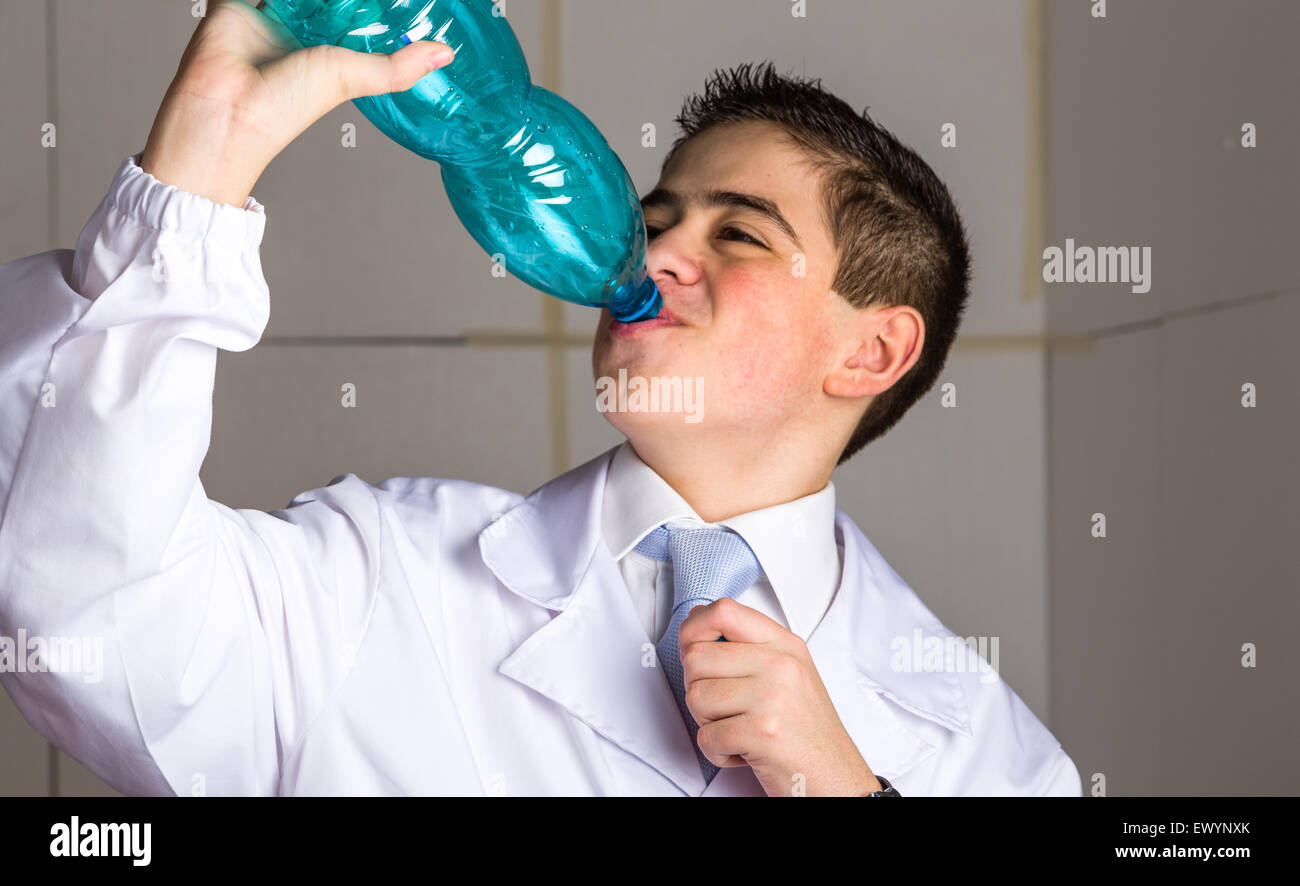 A boy doctor in blue tie and white coat  drinking water from plastic bottle. His acne skin has not ben retouched Stock Photo
