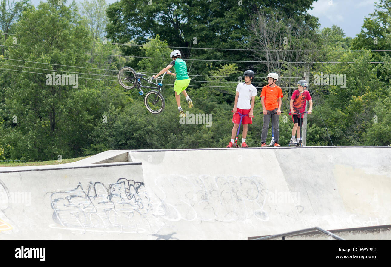 Three teenage boys watch another teenage boy do a stunt with his bmx bike at a skateboard park. Stock Photo