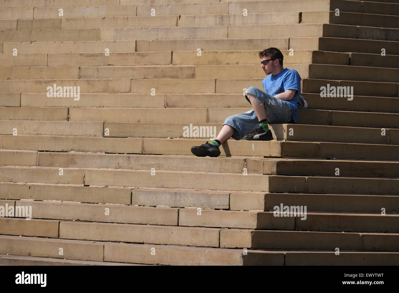 Male sat on the stone steps of Bolton Town Hall in the UK Stock Photo