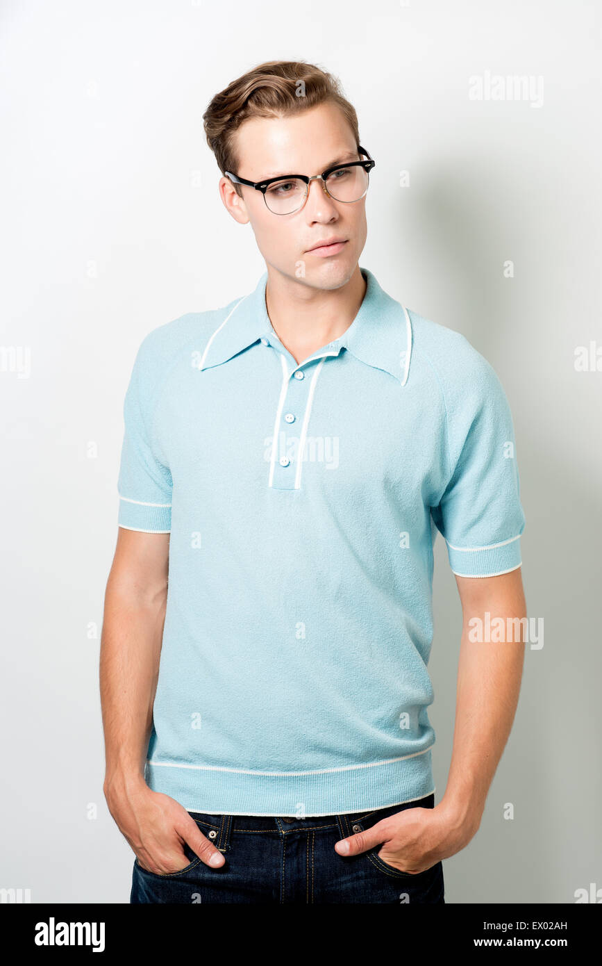 A handsome young man wearing 50s eye glasses and vintage top, posing with hands in pocket, looking away Stock Photo