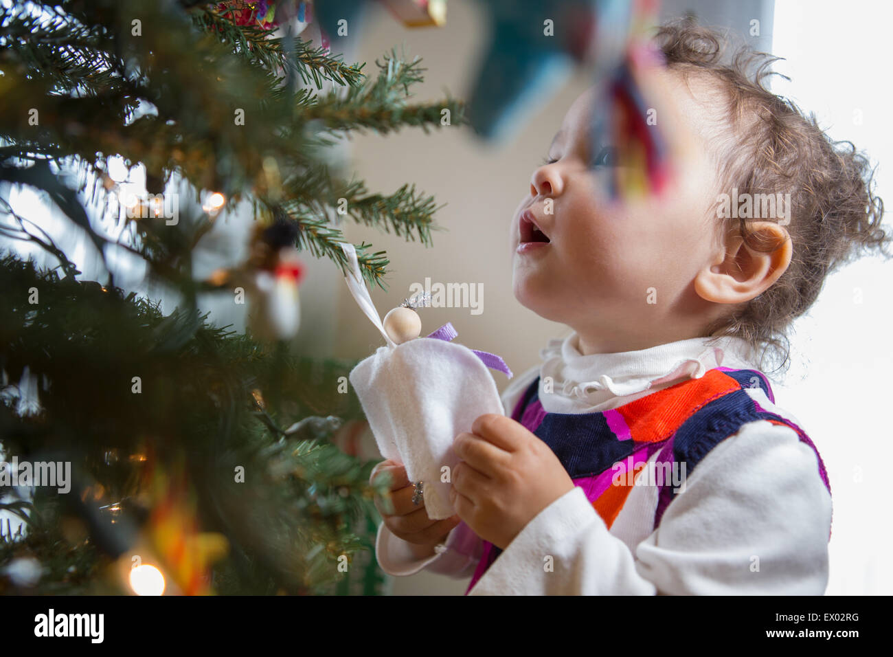 Little girl looking at angel ornament on Christmas tree Stock Photo