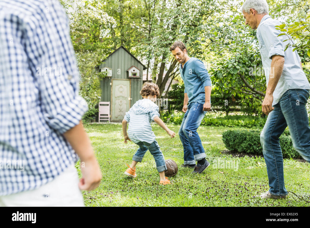 Mature man and son playing soccer with grandsons in garden Stock Photo