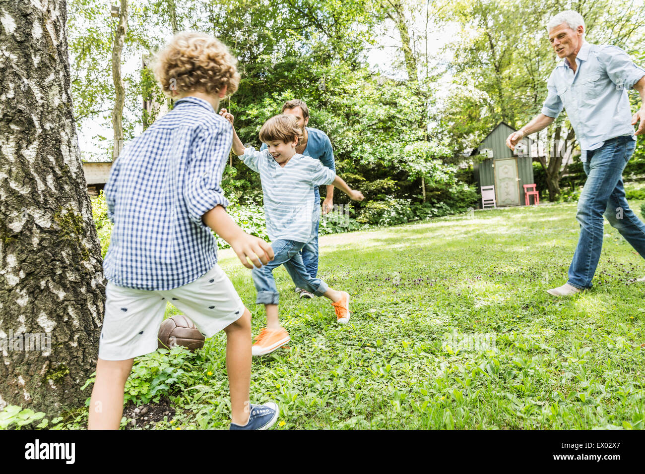 Mid adult man and father playing garden soccer with sons Stock Photo